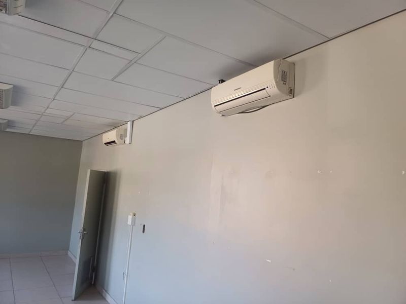 An empty office space featuring a suspended ceiling, tiled flooring, and dual wall-mounted air conditioning units.