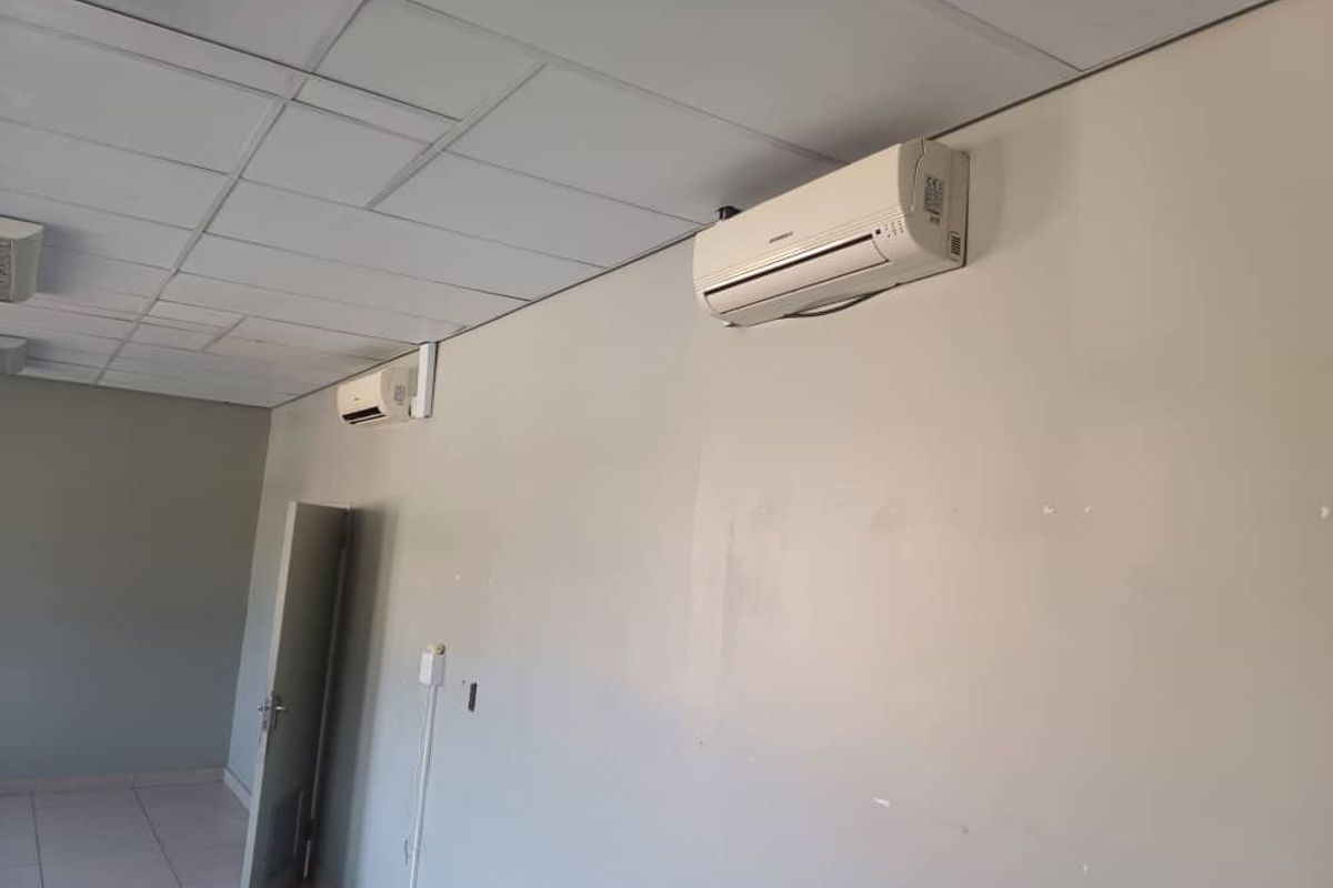 An empty office space featuring a suspended ceiling, tiled flooring, and dual wall-mounted air conditioning units.