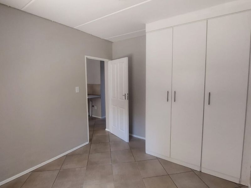A clean, empty bedroom featuring neutral grey walls, tiled flooring, and a spacious built-in wardrobe with white cabinetry.