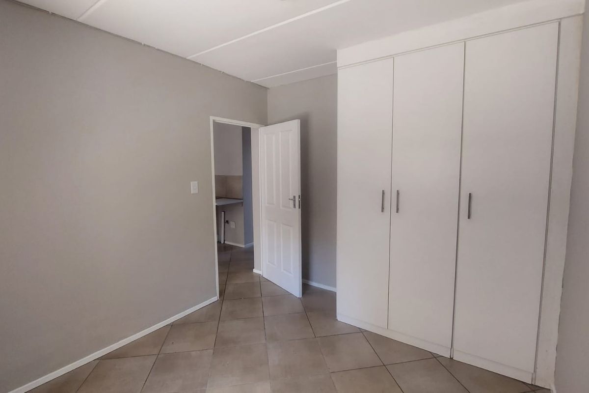 A clean, empty bedroom featuring neutral grey walls, tiled flooring, and a spacious built-in wardrobe with white cabinetry.