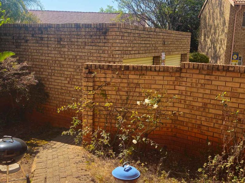 A rear exterior view of the townhouse featuring a paved walkway, face brick boundary walls, and access to the garage structure.