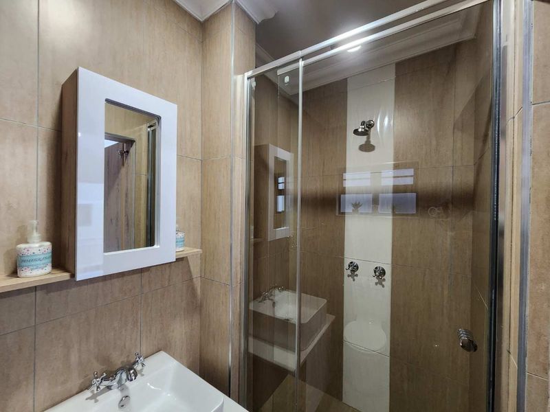Modern bathroom featuring a glass-enclosed shower, wall-mounted basin, and neutral-toned tiled walls, offering a clean and functional space.