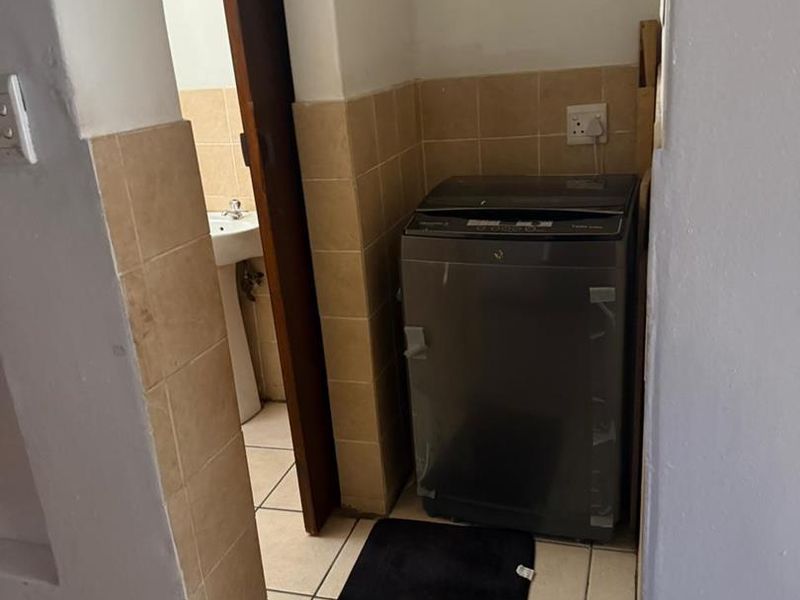 A functional laundry area featuring tiled flooring and splashback, with direct access to an adjacent bathroom space.
