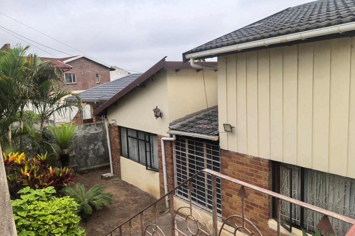 Rear view of the property showing brick and painted wall finishes, tiled roofing, and metal security features with an adjacent garden area.
