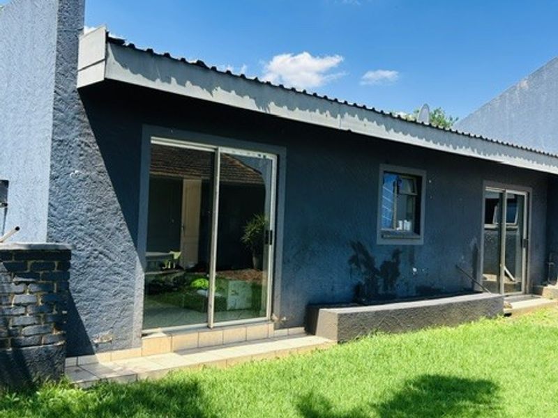 Rear exterior view of the house featuring sliding glass doors, a small tiled patio area, and a well-maintained lawn.