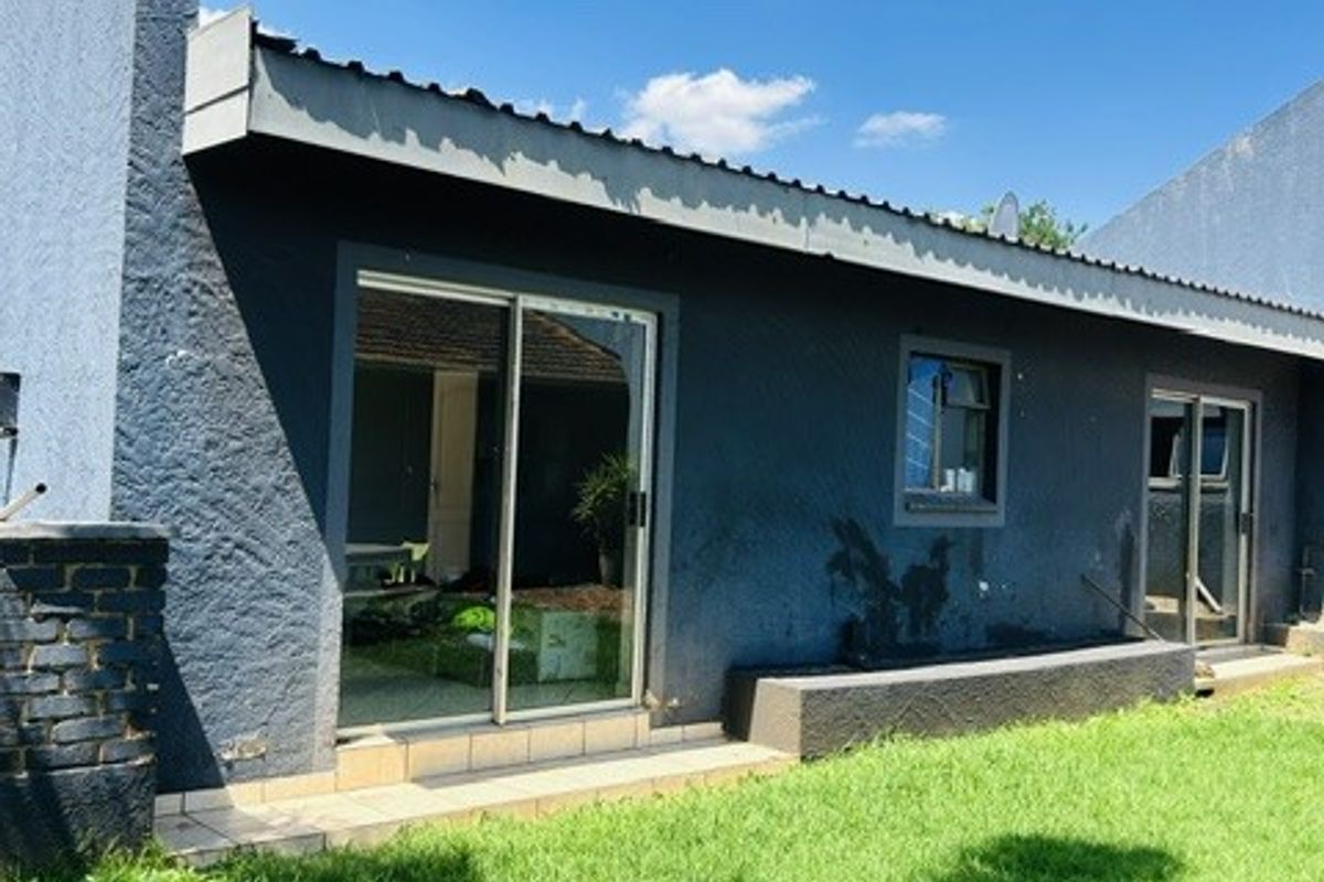 Rear exterior view of the house featuring sliding glass doors, a small tiled patio area, and a well-maintained lawn.