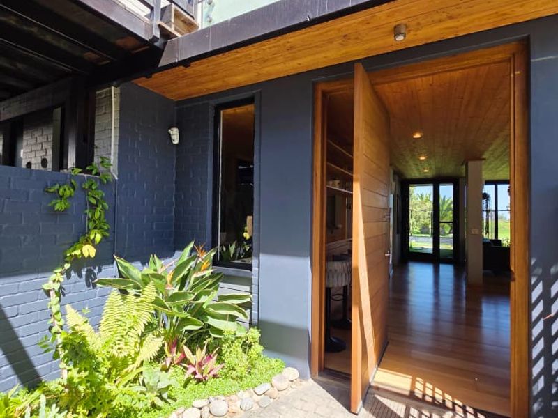 Modern entrance featuring a large timber pivot door, glass balustrade, and timber-clad ceiling, leading into a bright, open-plan living space.