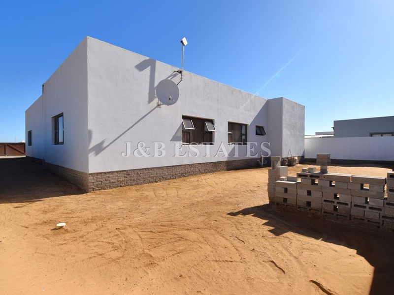 Rear view of the property showing the exterior wall, satellite dish, and an unfinished sandy backyard area with a low brick boundary wall.