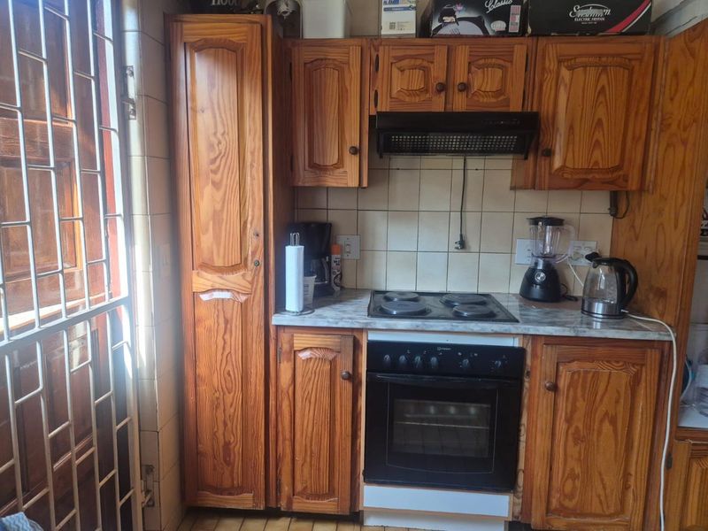 A compact kitchen featuring traditional wooden cabinetry, a built-in oven with electric hob, and tiled backsplash, offering a functional but dated layout.