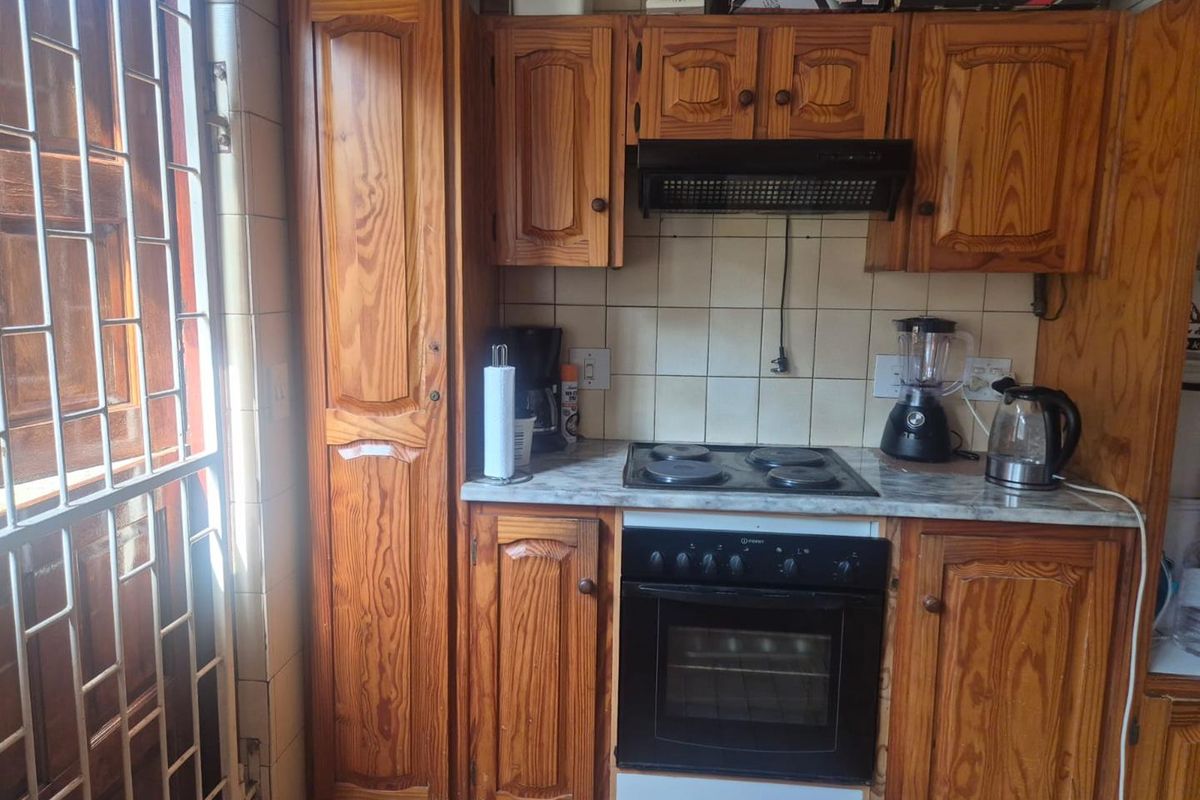 A compact kitchen featuring traditional wooden cabinetry, a built-in oven with electric hob, and tiled backsplash, offering a functional but dated layout.