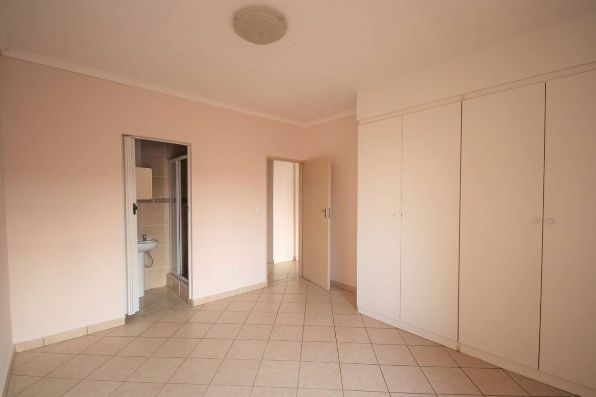 A spacious, empty bedroom featuring neutral tiled flooring, built-in cupboards, and direct access to an en-suite bathroom.