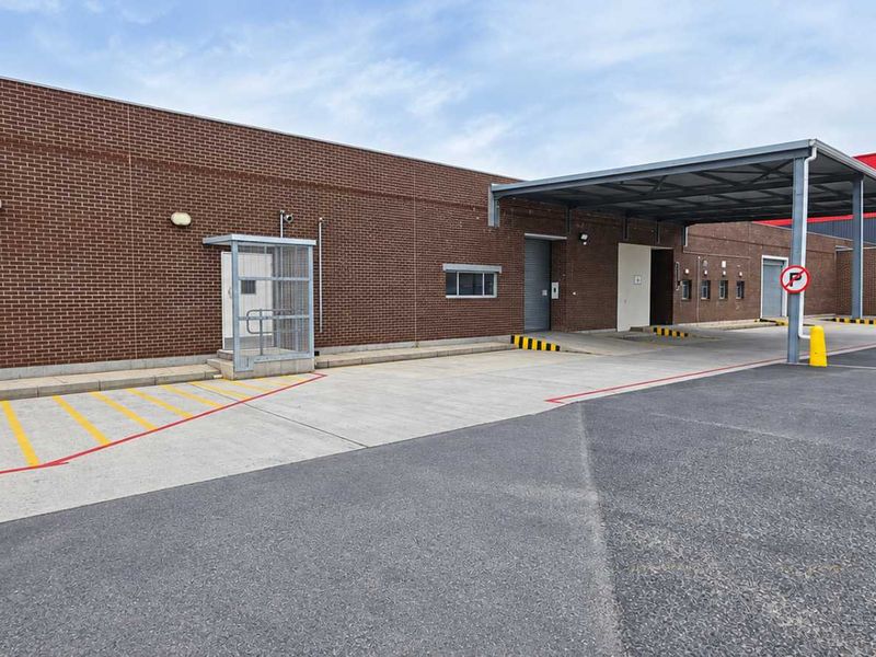 Industrial property exterior featuring a brick facade, covered loading bay area, and paved driveway with clear access points.