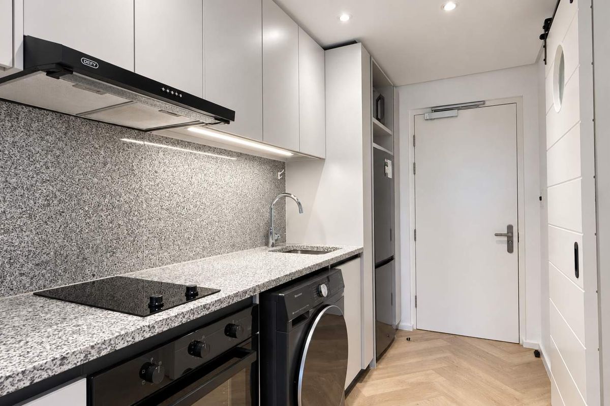 Modern kitchen featuring granite countertops, built-in oven, electric hob, extractor fan, and herringbone wood flooring, offering a sleek and functional culinary space.
