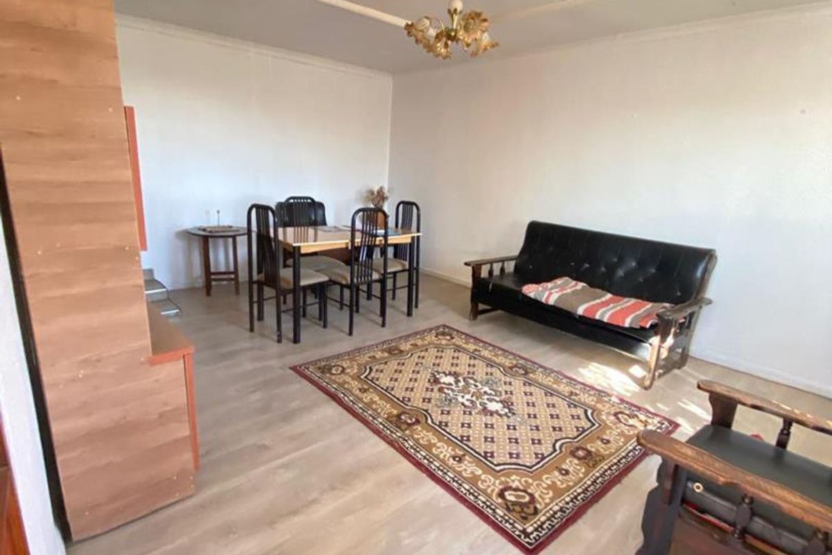 A spacious living and dining area featuring light-toned laminate flooring and a decorative ceiling rose with a central chandelier.