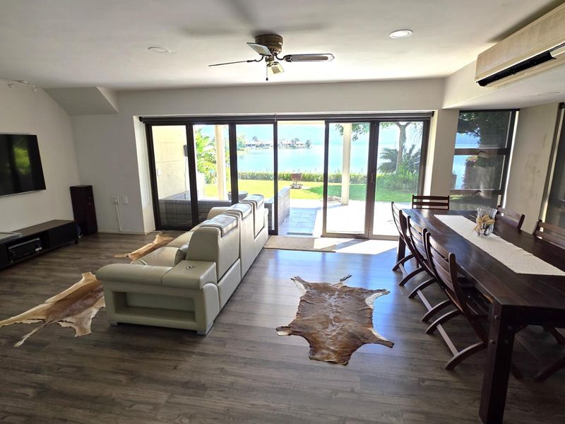 Spacious open-plan living and dining area featuring laminate flooring, ceiling fan, and large sliding glass doors providing direct access to the patio and lake view.