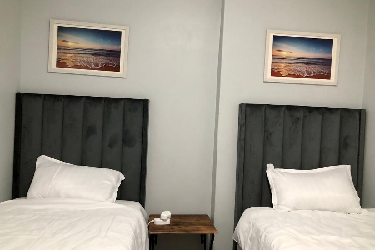 A bedroom featuring two twin beds with dark upholstered headboards and neutral wall finishes.