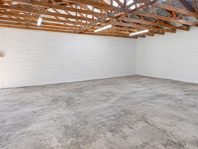 Spacious industrial utility area featuring exposed timber roof trusses, durable concrete flooring, and painted block walls, suitable for storage or workshop use.