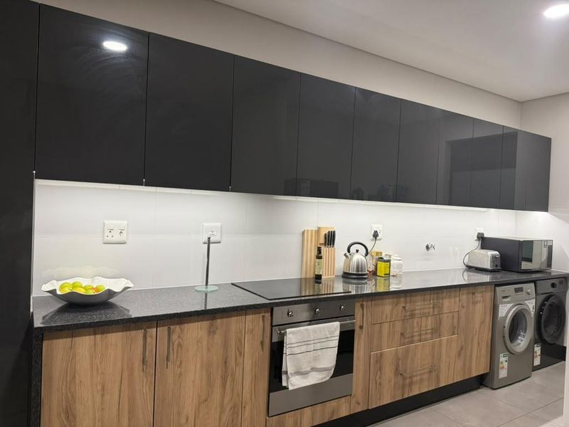 Modern kitchen featuring high-gloss black upper cabinets, wood-grain lower cabinetry, granite countertops, built-in oven, electric hob, and integrated laundry facilities.