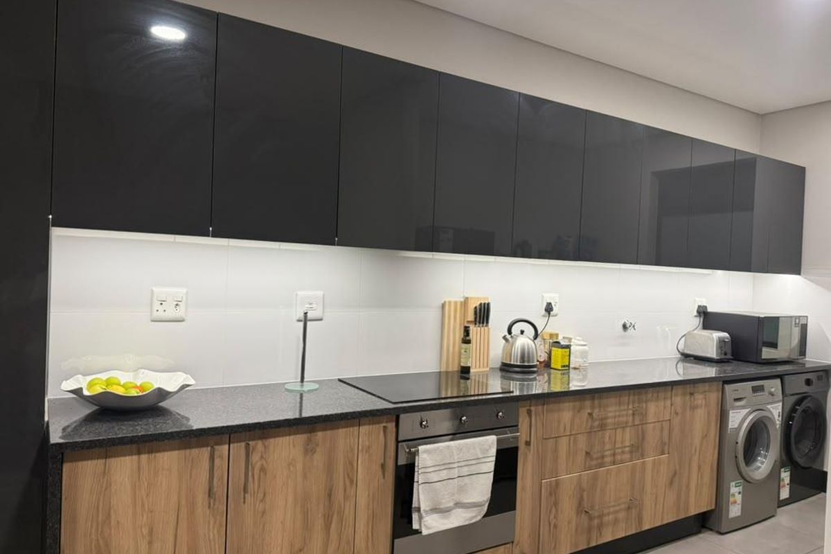 Modern kitchen featuring high-gloss black upper cabinets, wood-grain lower cabinetry, granite countertops, built-in oven, electric hob, and integrated laundry facilities.