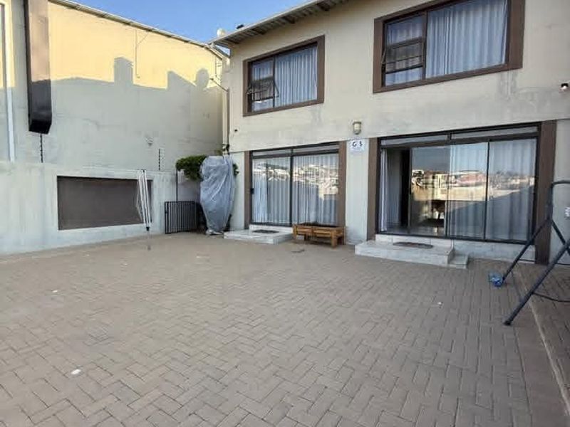 Rear exterior view featuring a paved courtyard, sliding glass doors providing access to the interior, and a multi-level building facade.