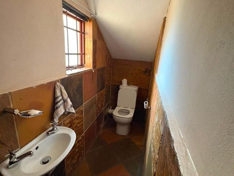 A compact bathroom featuring a wall-mounted basin, toilet, and dated tiled finishes under a sloped ceiling.