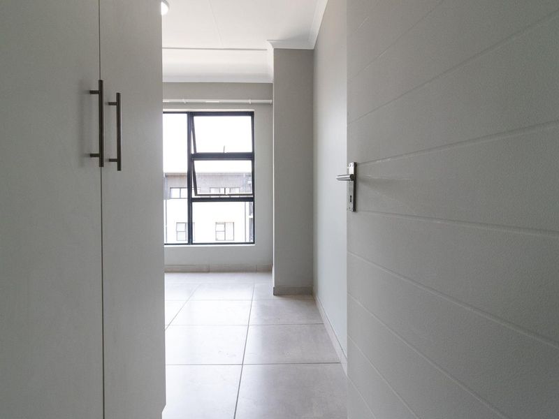 A bright, empty bedroom featuring neutral tiled flooring, built-in cupboards, and a modern aluminium window frame.