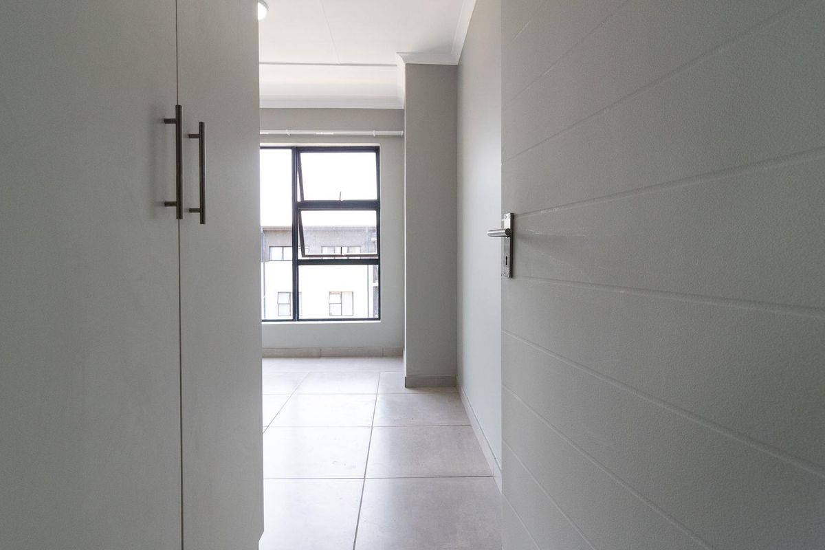 A bright, empty bedroom featuring neutral tiled flooring, built-in cupboards, and a modern aluminium window frame.