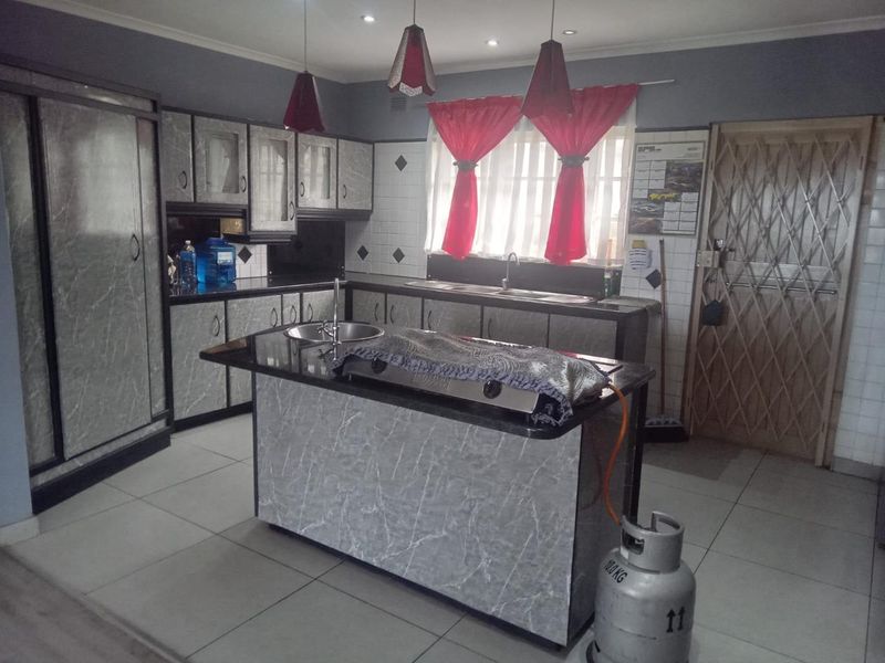 Kitchen featuring marble-effect cabinetry, granite countertops, a central island with a sink, and tiled flooring.