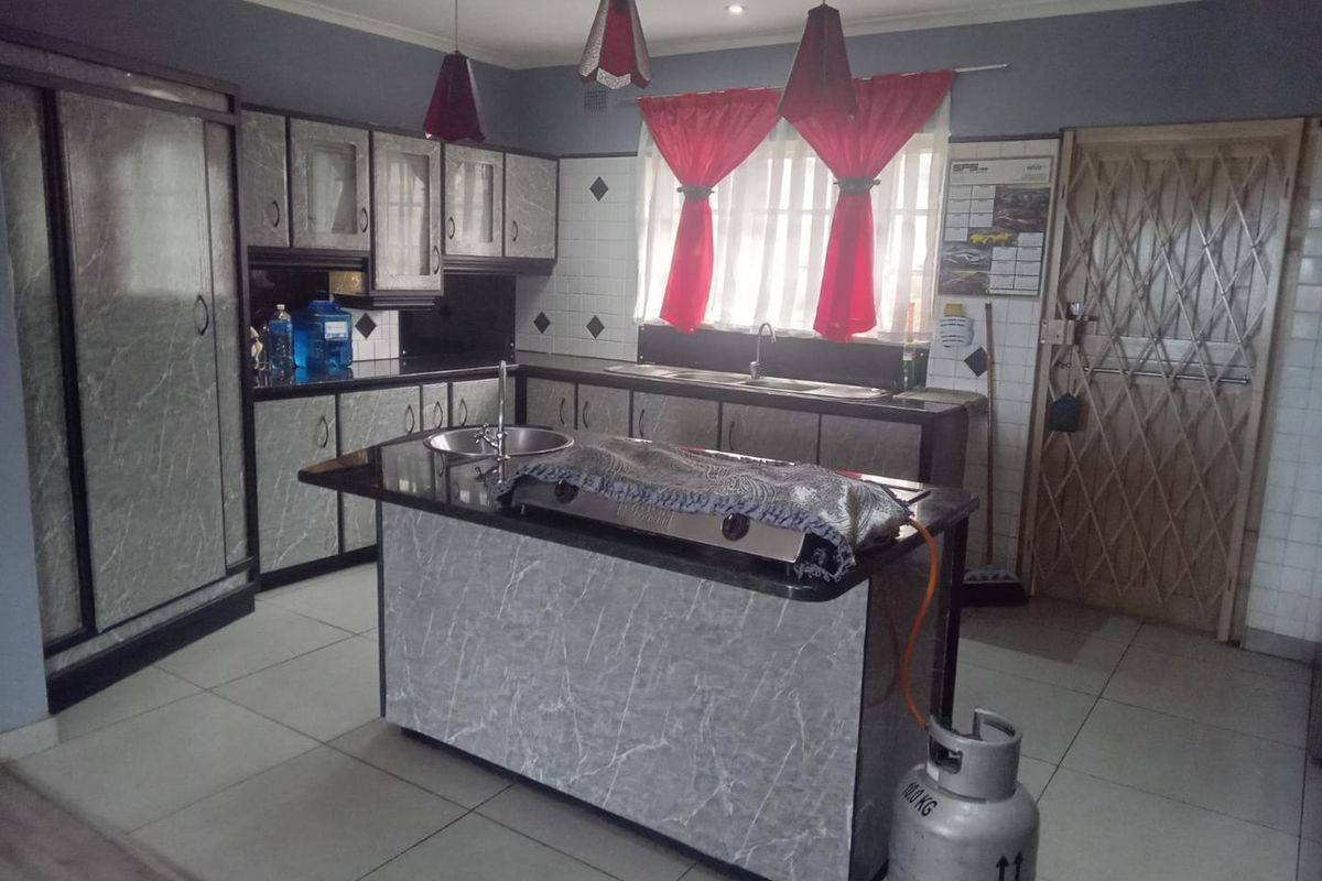 Kitchen featuring marble-effect cabinetry, granite countertops, a central island with a sink, and tiled flooring.