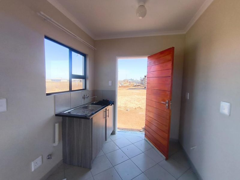 A compact, functional kitchen area featuring a single sink unit, built-in cabinetry, tiled flooring, and direct access to the exterior.