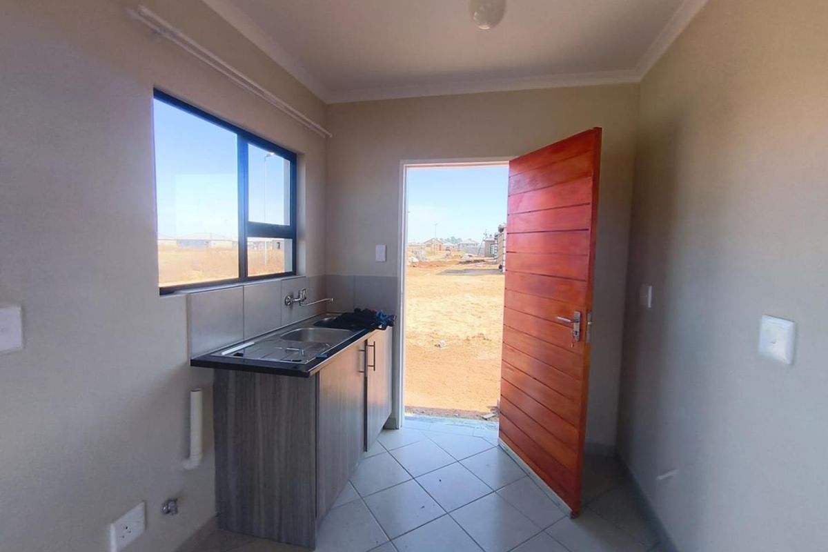 A compact, functional kitchen area featuring a single sink unit, built-in cabinetry, tiled flooring, and direct access to the exterior.