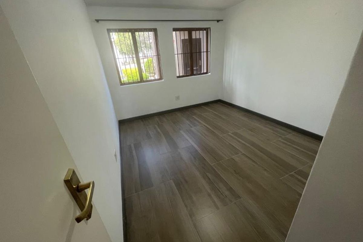 An empty bedroom featuring wood-look tiled flooring and windows fitted with security bars.