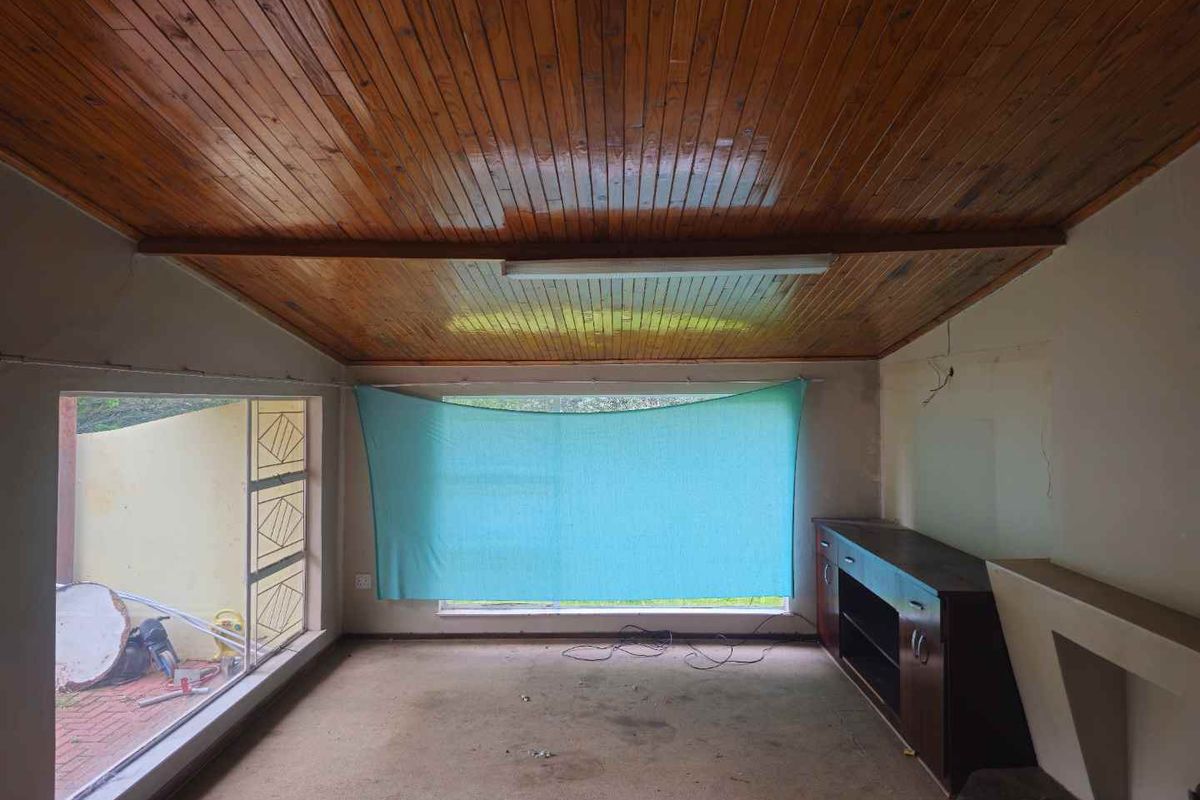 A living room featuring a timber-clad ceiling, large windows, and built-in cabinetry, currently in need of cosmetic updates and flooring replacement.