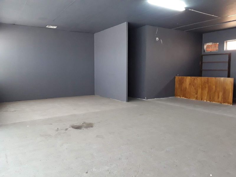 An open-plan commercial space featuring dark grey painted walls, concrete flooring, and a built-in wooden service counter.