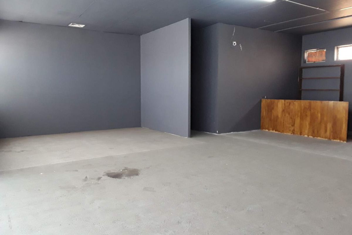 An open-plan commercial space featuring dark grey painted walls, concrete flooring, and a built-in wooden service counter.