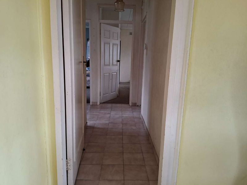 A functional hallway featuring tiled flooring and access to multiple rooms, showing signs of wear and dated finishes.