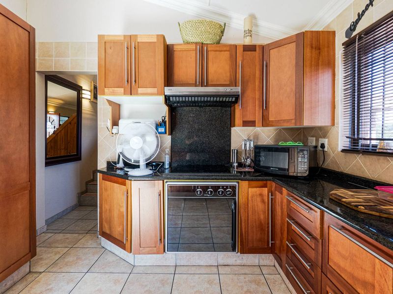 A functional kitchen featuring warm-toned wooden cabinetry, granite countertops, a built-in oven, and tiled finishes throughout.