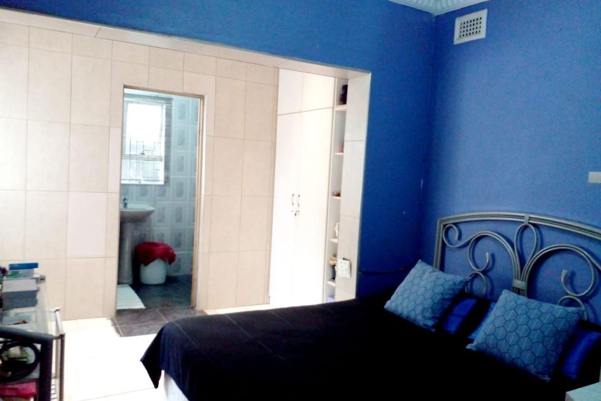 A bedroom featuring blue walls, tiled flooring, and an adjoining en-suite bathroom with a pedestal basin and built-in storage.