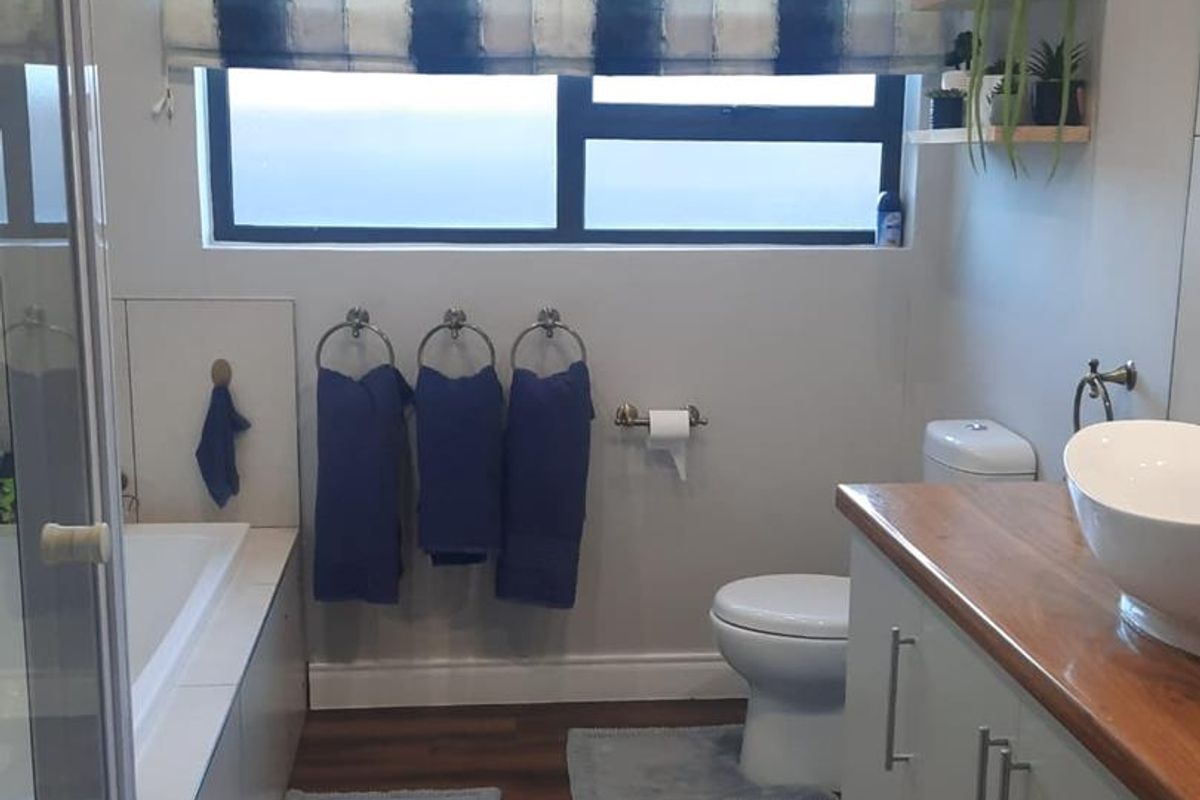A well-maintained bathroom featuring a built-in bathtub, separate shower enclosure, modern vessel sink on a timber vanity, and a toilet.