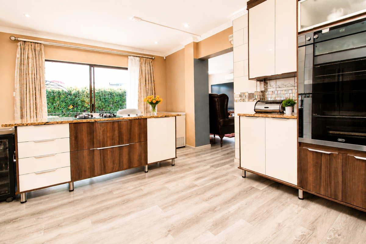 Modern kitchen featuring two-tone cabinetry, granite countertops, integrated oven, and a gas hob, with wood-look laminate flooring and direct access to the living area.