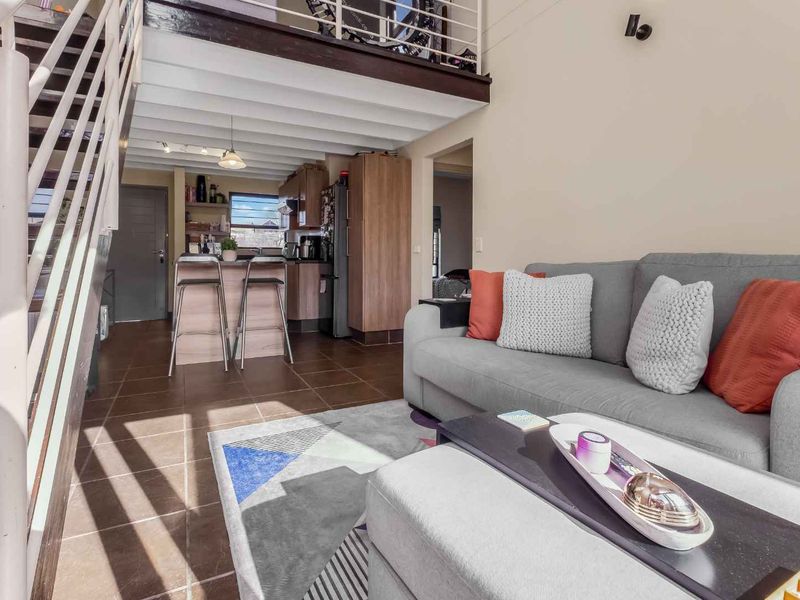 Open-plan living area featuring a mezzanine level, staircase, and integrated kitchen with a breakfast counter, finished with tiled flooring throughout.