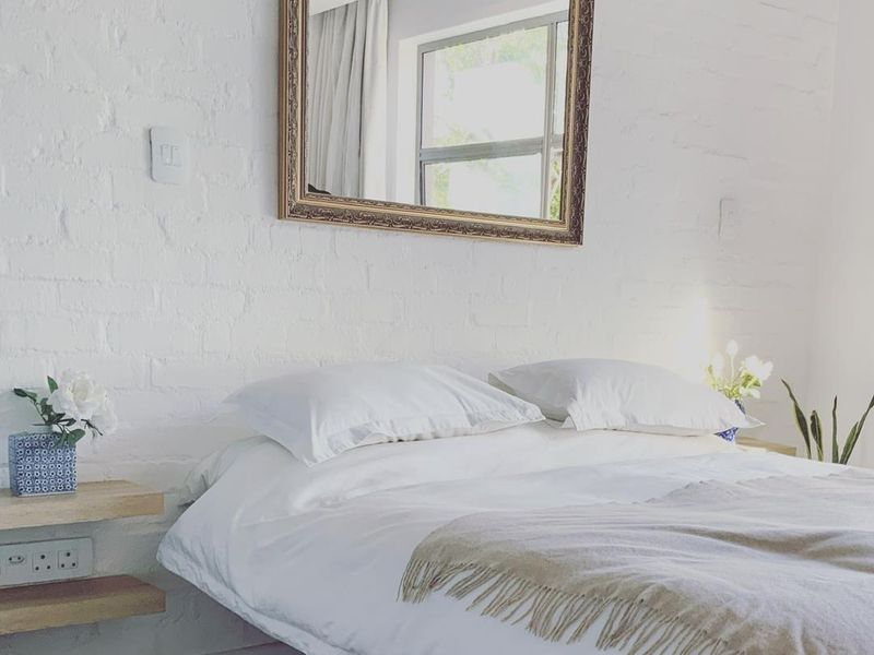 A bright bedroom featuring a white painted exposed brick wall, floating wooden bedside shelves, and integrated electrical outlets.