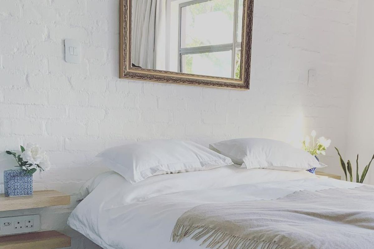 A bright bedroom featuring a white painted exposed brick wall, floating wooden bedside shelves, and integrated electrical outlets.