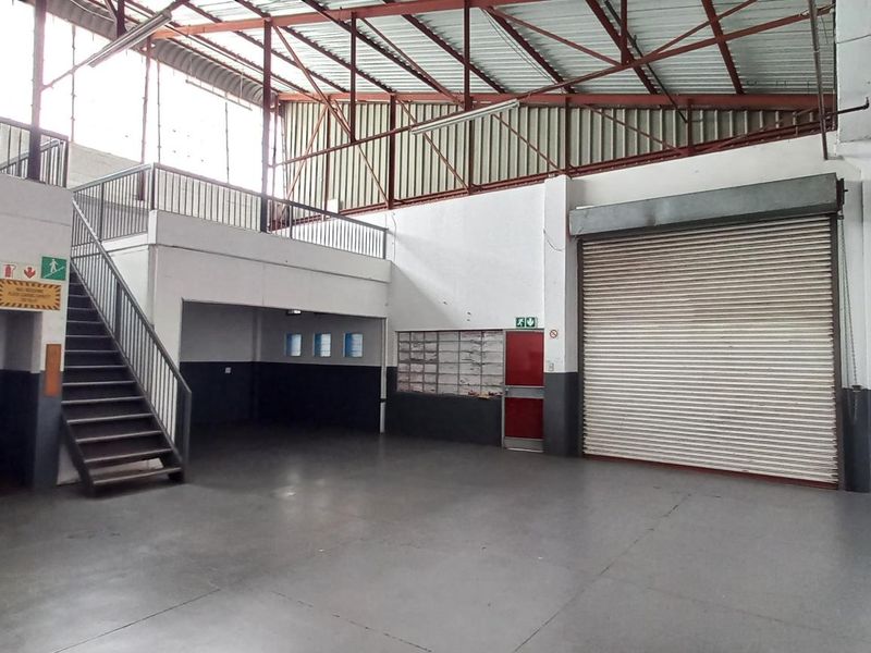 Spacious industrial warehouse unit featuring a high-clearance ceiling, roller shutter door access, and a functional mezzanine level suitable for office or storage use.