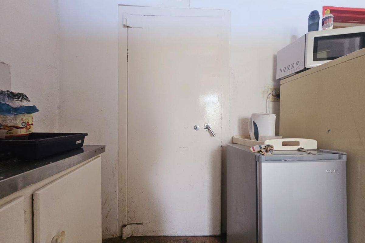 A functional utility or kitchen area featuring basic cabinetry, a stainless steel sink unit, and a secure access door.