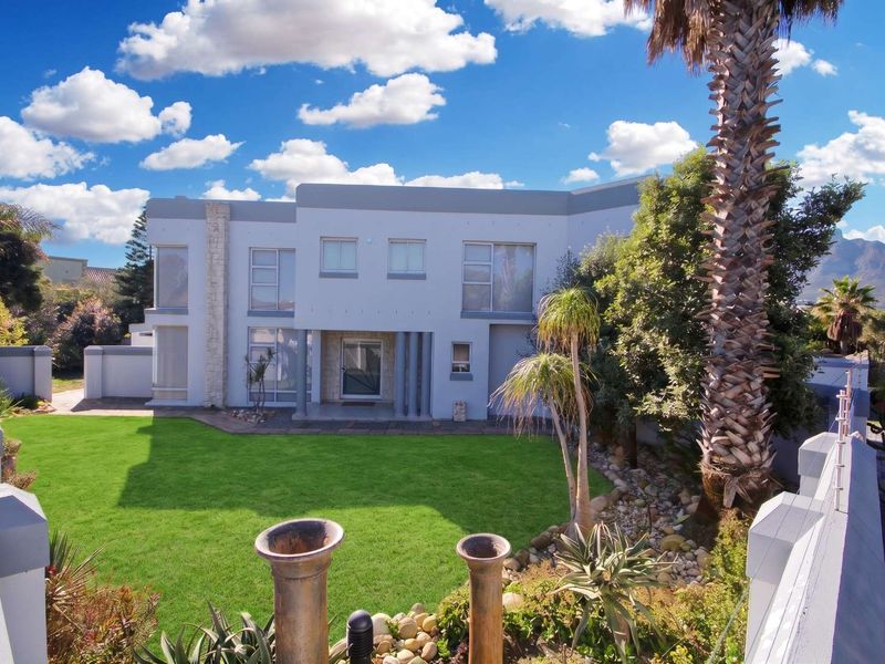 A well-maintained double-story residence featuring modern architectural lines, stone accents, large glass windows, and a spacious, manicured rear garden.