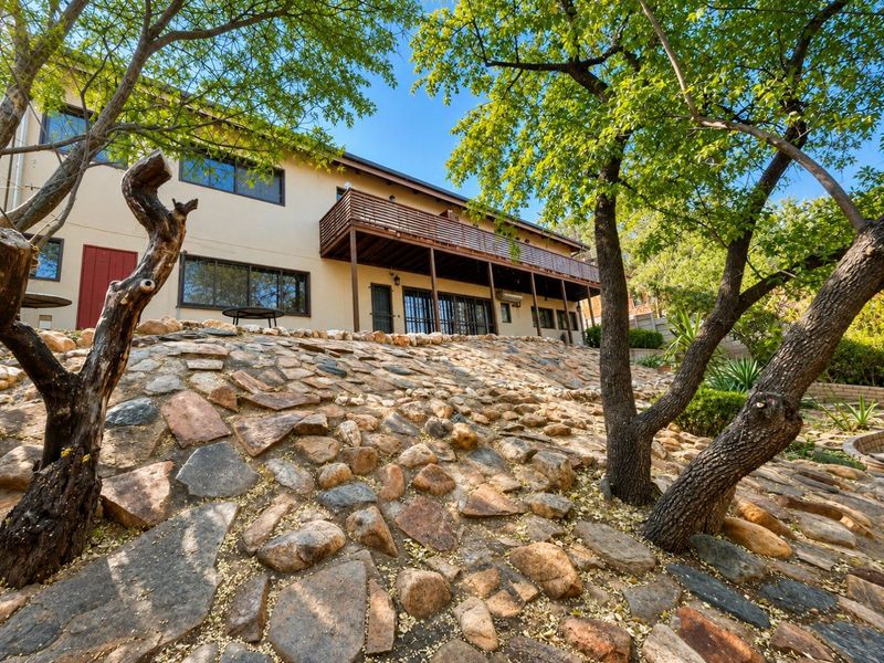 Rear view of the property featuring a raised wooden deck, stone retaining wall landscaping, and sliding door access to the home.