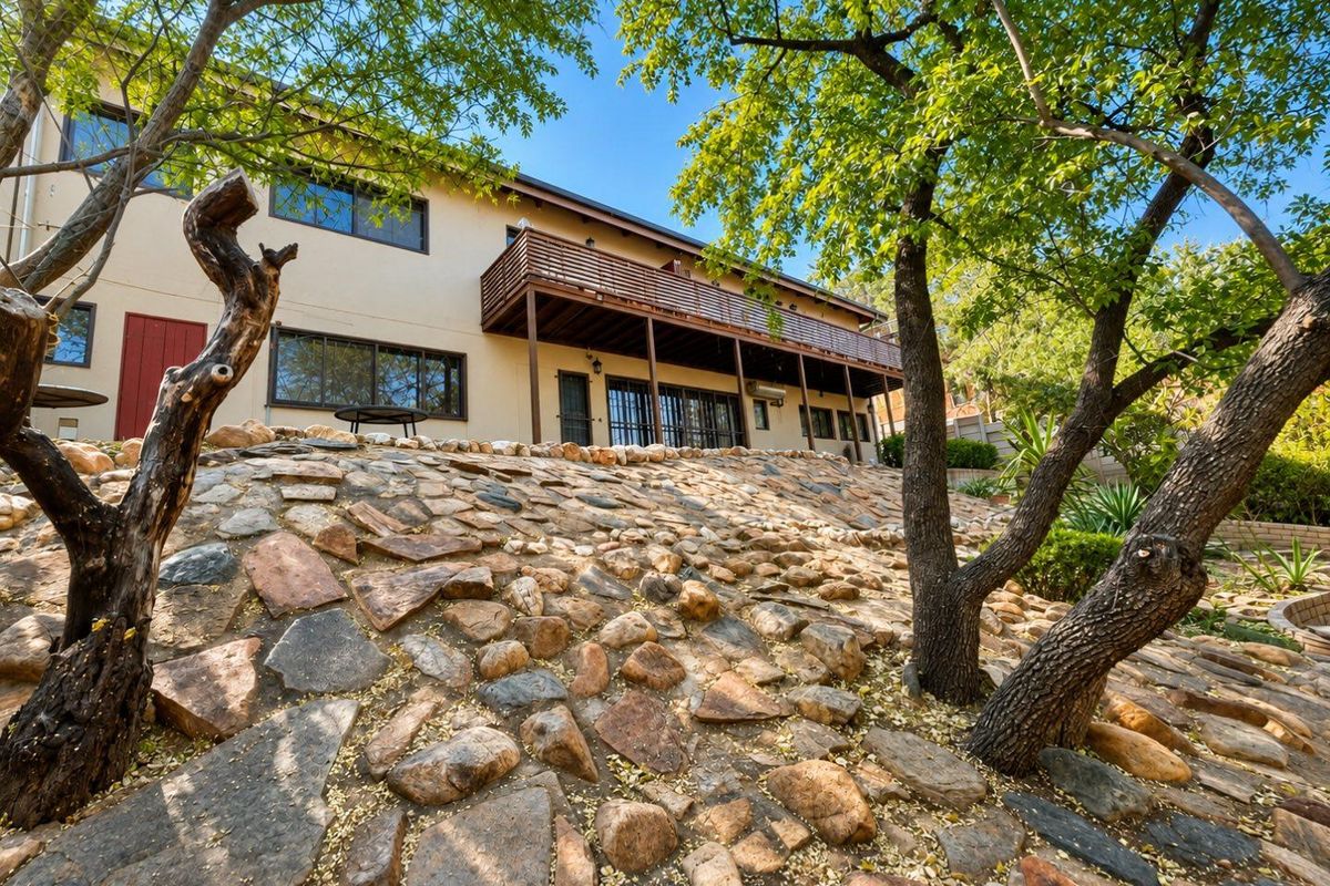 Rear view of the property featuring a raised wooden deck, stone retaining wall landscaping, and sliding door access to the home.