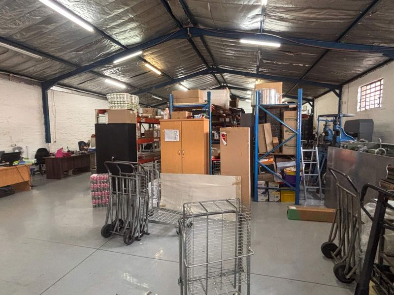 Spacious industrial utility area featuring exposed steel roof trusses, durable epoxy-coated concrete flooring, and functional industrial shelving units suitable for storage or workshop use.