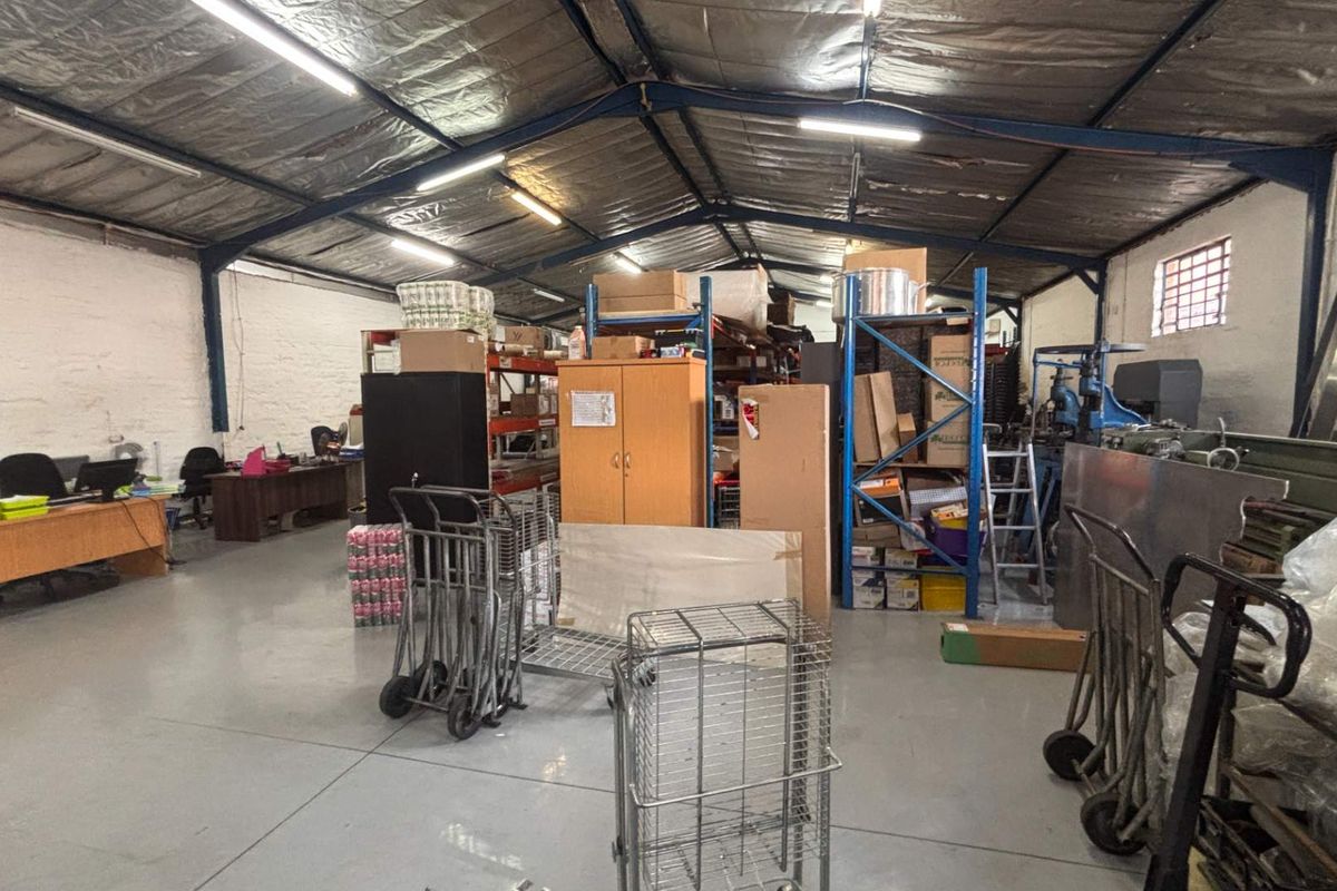 Spacious industrial utility area featuring exposed steel roof trusses, durable epoxy-coated concrete flooring, and functional industrial shelving units suitable for storage or workshop use.